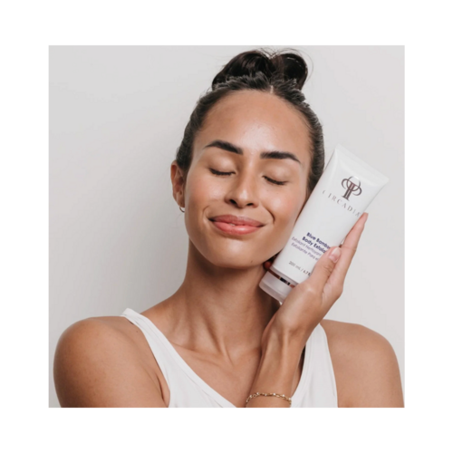 Smilende kvinde, der holder Circadia Blue Bamboo Exfoliator, og fremmer dens fordele som en kropsscrub for glat, sundt udseende hud.