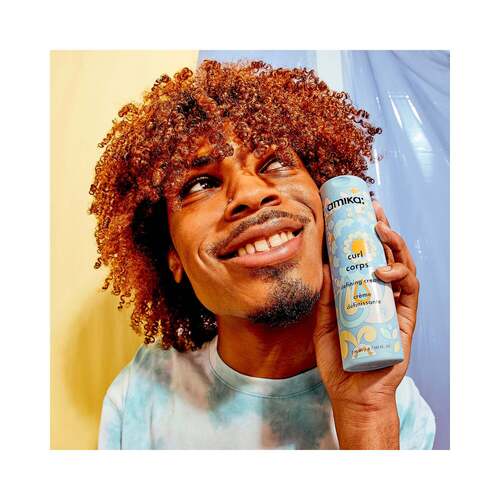 Curly-haired person holding Amika Curl Corps Defining Cream, demonstrating its effectiveness in curl definition and softness.