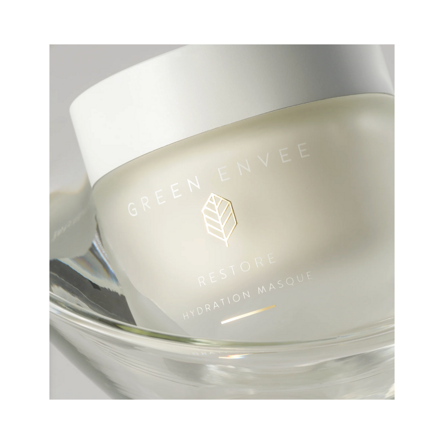 ガラス皿に入った Green Envee Restore Hydration Masque ジャーの斜めから見た図。プレミアム スキンケアのプレゼンテーションを強調しています。
