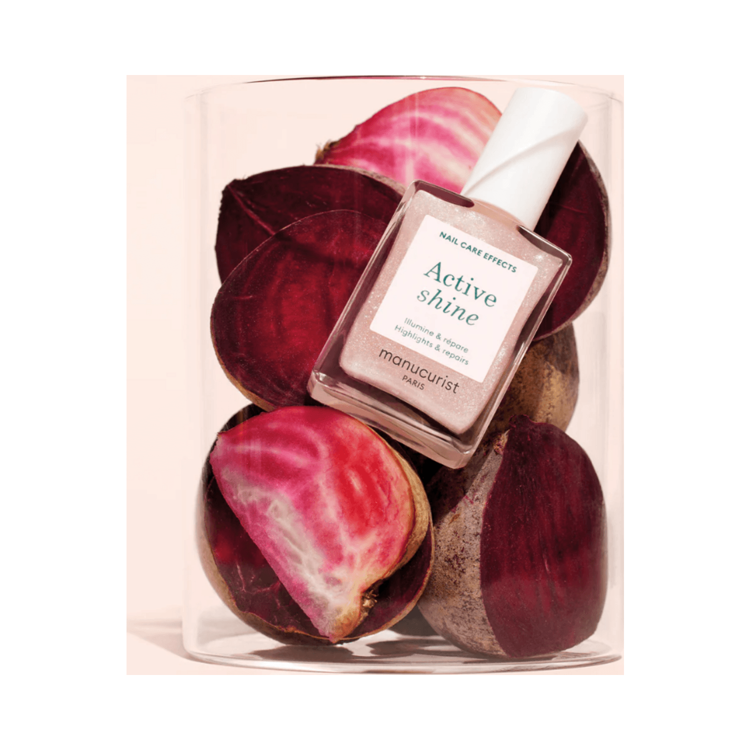 Manucurist Active Shine nail polish displayed in a glass container filled with sliced beets, highlighting its plant-based ingredients.