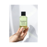Hand holding Olverum Bath Oil bottle in natural light. A luxurious body oil for calming and aromatic bath experiences.