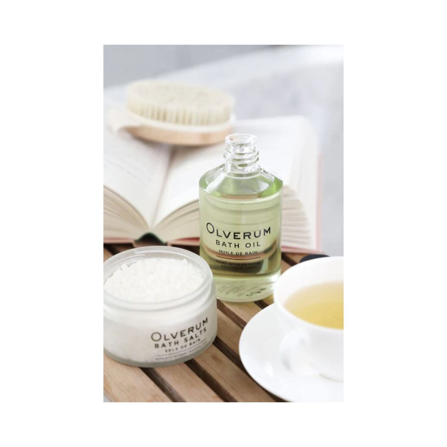 Open Olverum Bath Oil bottle beside bath salts and tea. A relaxing bath oil ideal for spa-like home rituals and body care.