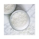 Top view of coarse white Olverum Bath Salts spilling from jar, a premium bath additive with magnesium and sea salt for soothing baths.