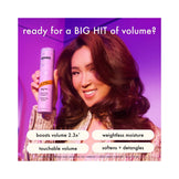 Woman with voluminous hair holding Amika Big Hit Volumizing Shampoo, promoting touchable volume, weightless moisture, and detangling benefits.