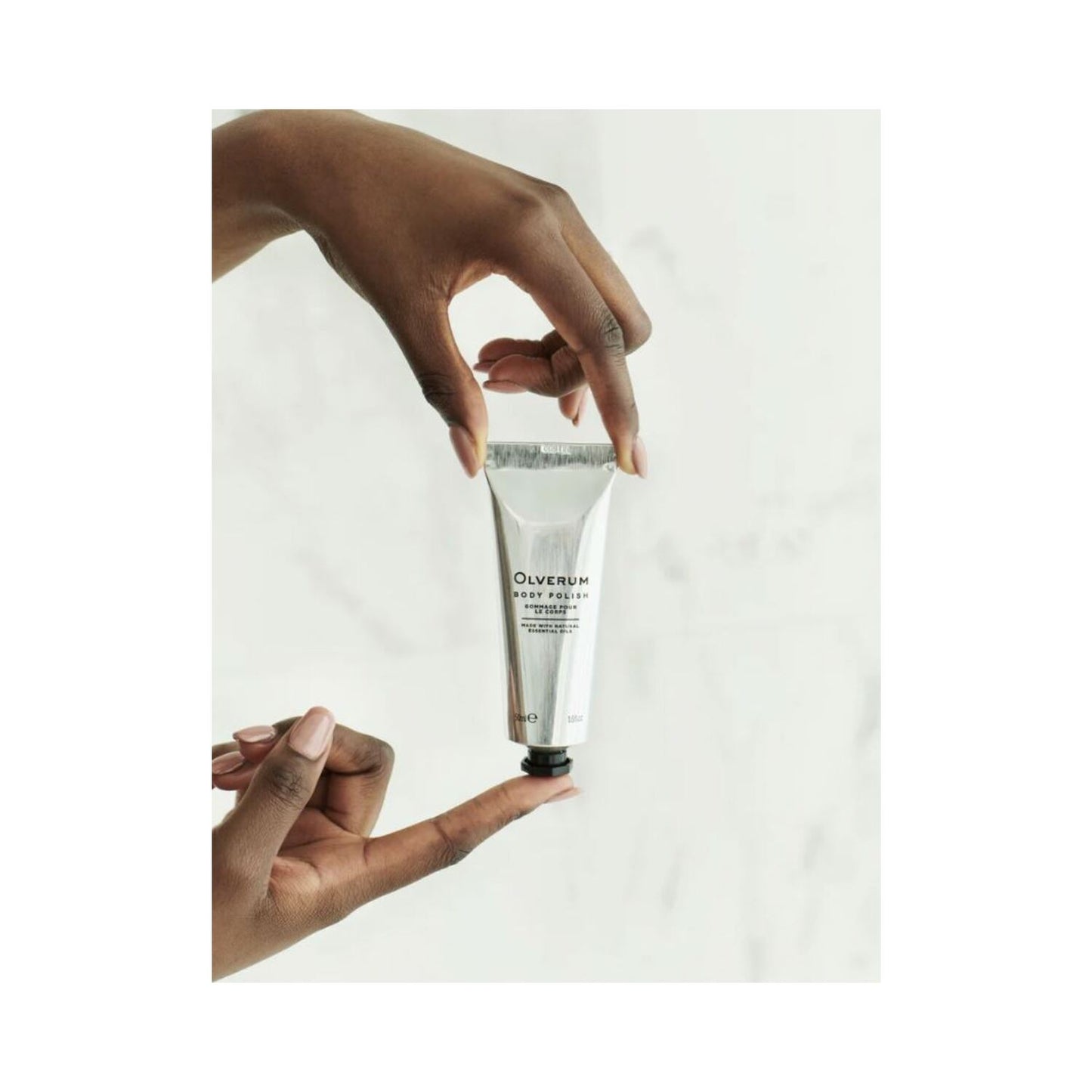 Olverum Body Polish applied to leg from silver tube. Smooth, exfoliating formula for radiant skin in bath and body care routines.