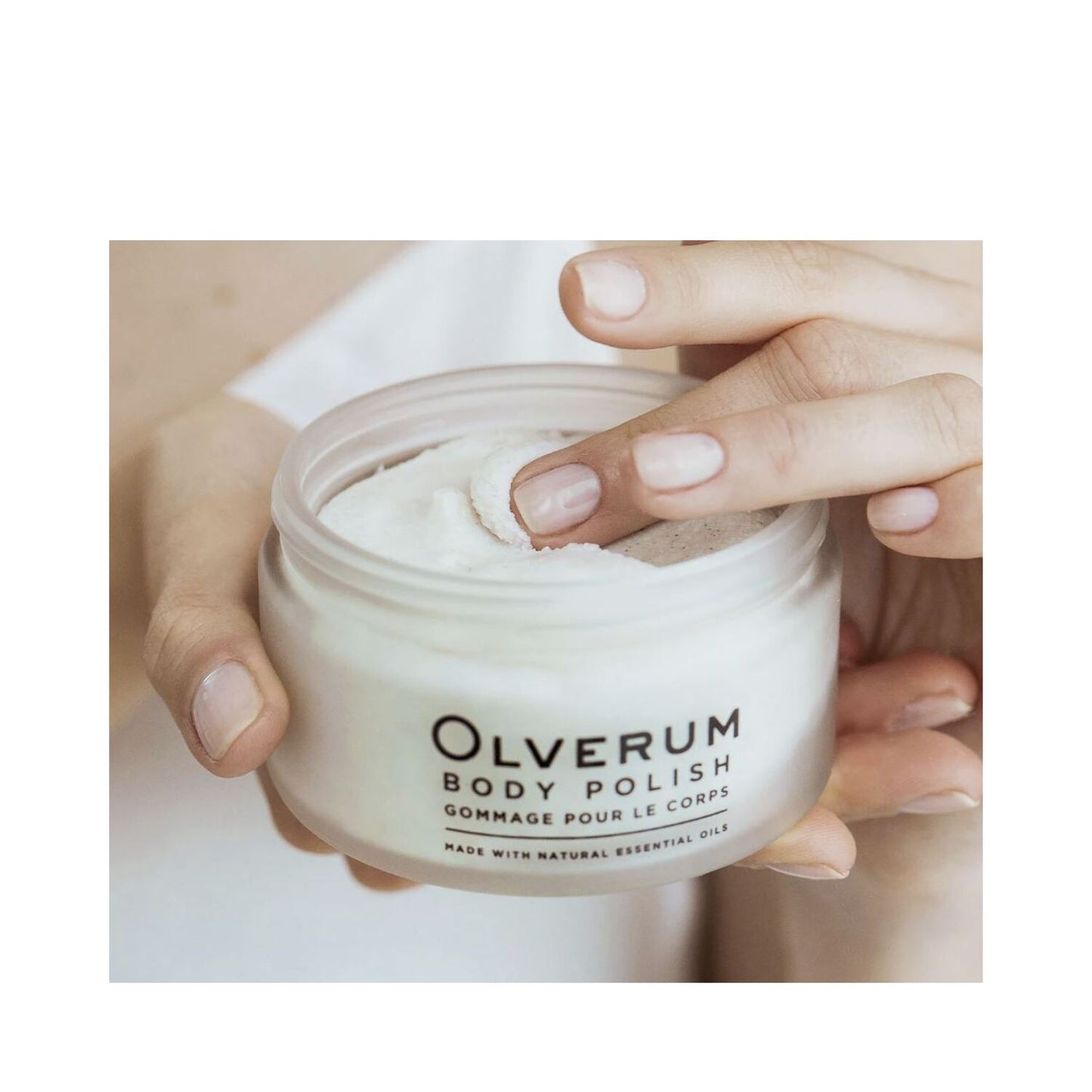 Woman applying Olverum Body Polish to shoulder area. Exfoliating body treatment for soft, nourished skin using natural ingredients.