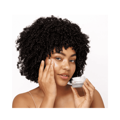 Model applying Omnilux CoQ10 Face Cream to face, showcasing its use for hydration and post-LED skincare treatment.