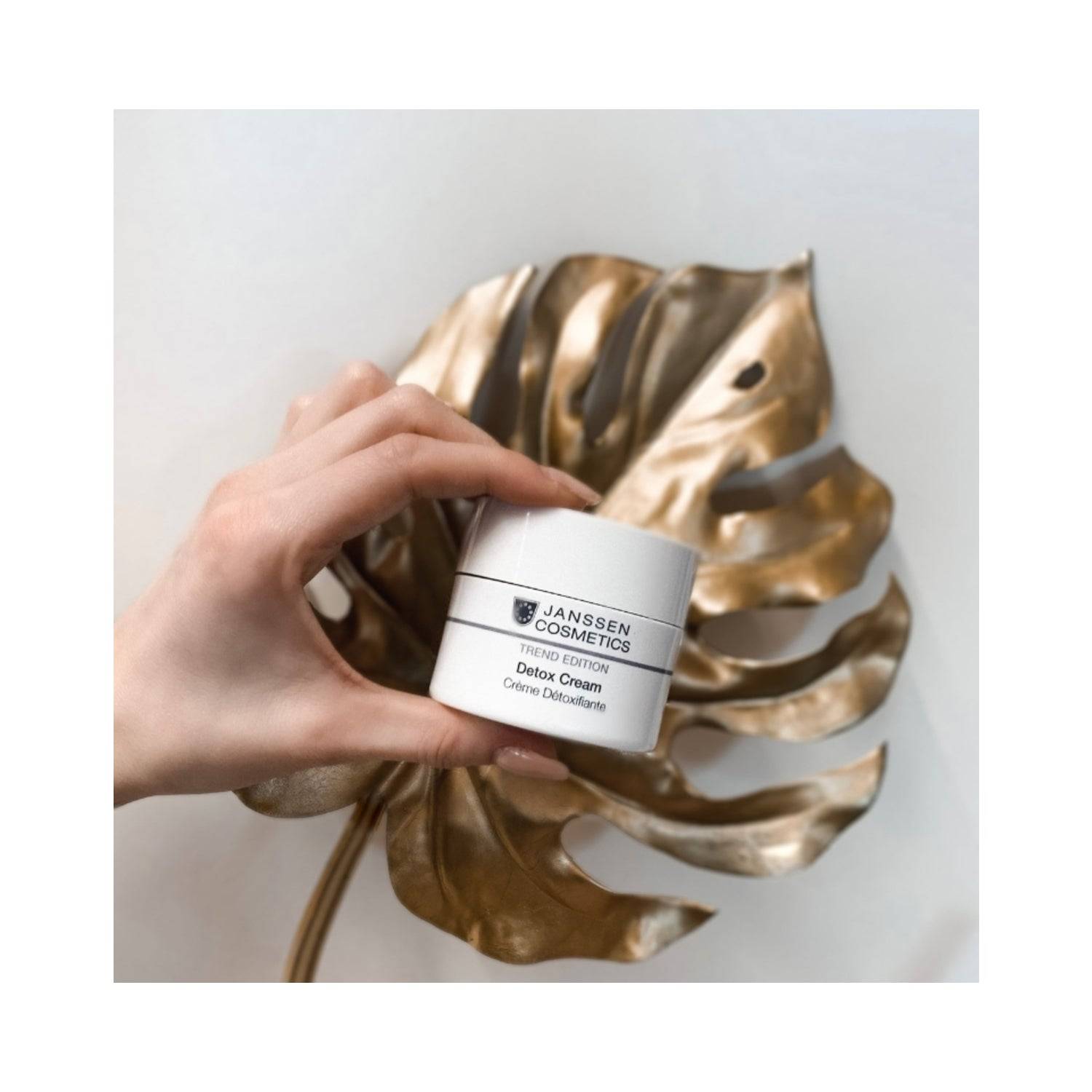 Hand holding Janssen Detox Face Cream jar over a decorative gold leaf, showcasing luxury skincare for detoxifying and moisturizing.