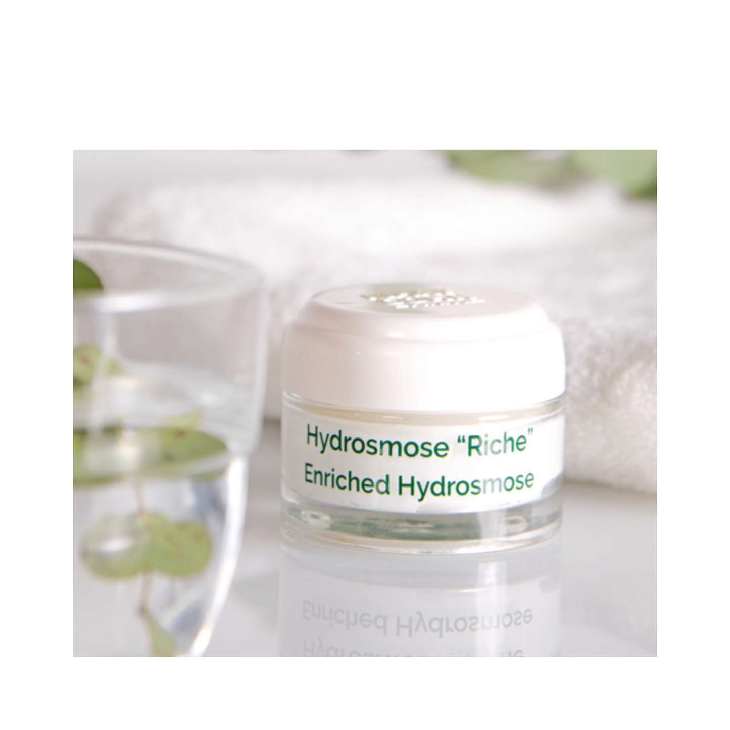 Mary Cohr Enriched Hydrosmose Moisturizer placed beside a glass of water and towel, emphasizing hydration and skincare luxury.