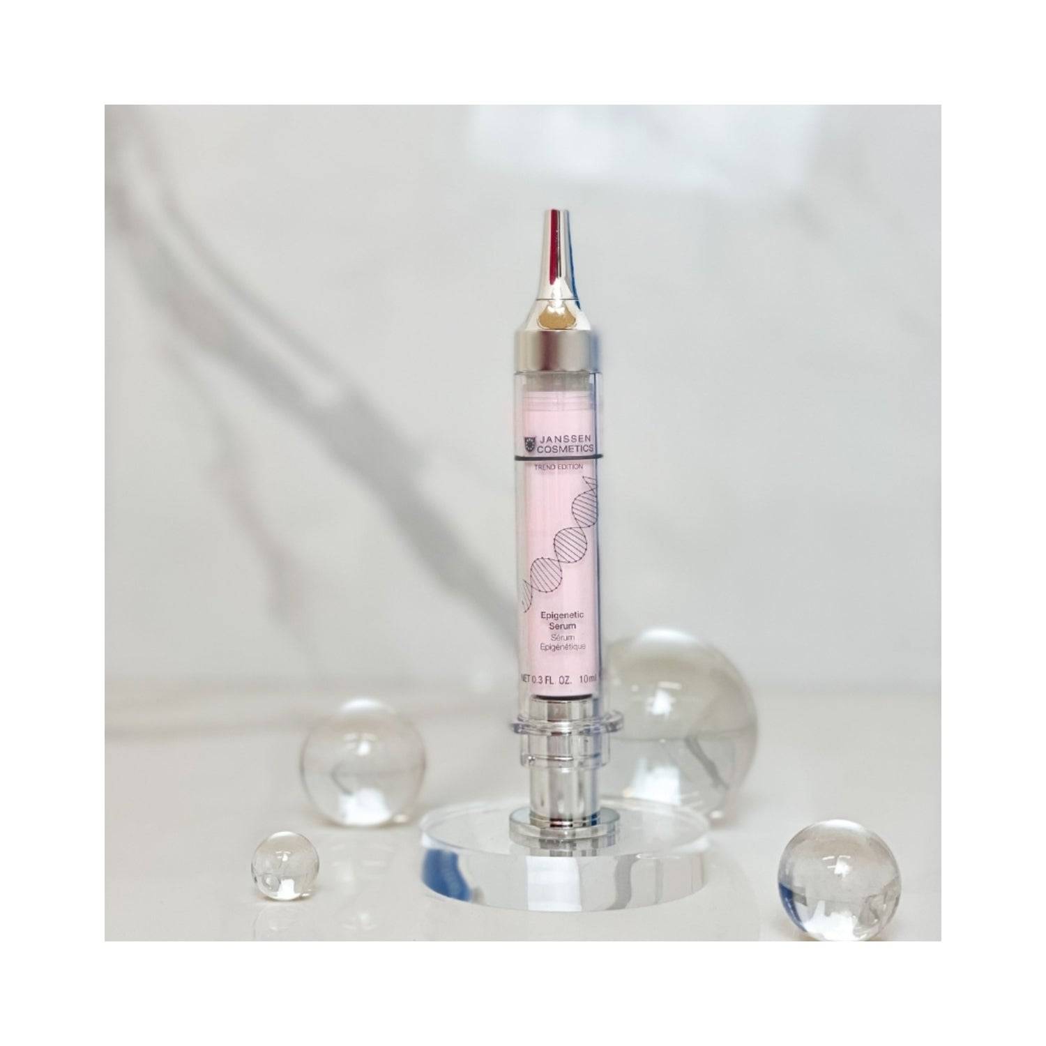 Janssen Epigenetic Serum displayed on a clear stand with decorative spheres. Premium face serum for resilient, youthful skin.