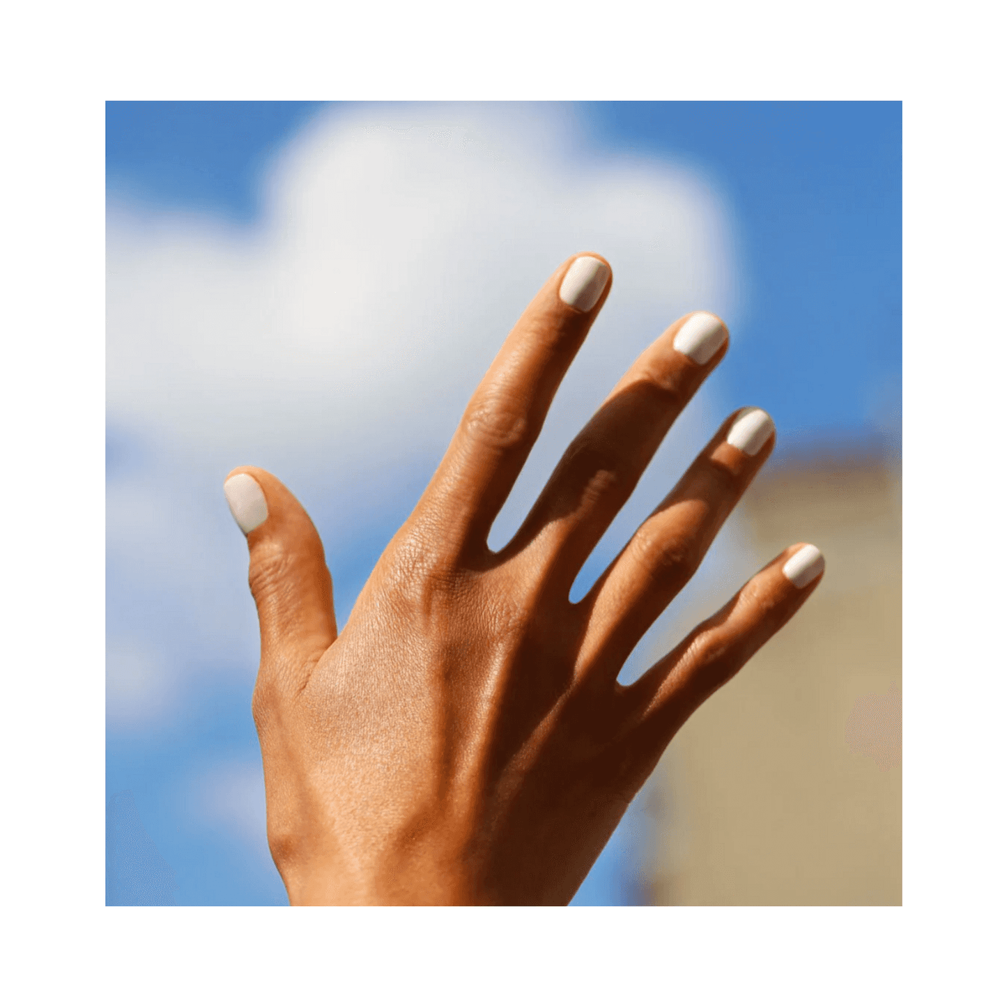 Hand with nails painted in Manucurist Green Flash Snow held up against a blue sky, highlighting the bright white polish.