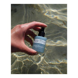 Hand holding Algologie Hydra-Replenish Booster serum above water, emphasizing its moisture-boosting formula for dry and dehydrated skin.