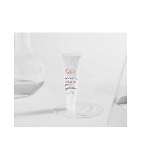Avene Hydrance Sunscreen SPF 30 tube displayed on a glass surface with lotion swatch, highlighting its lightweight, hydrating formula.