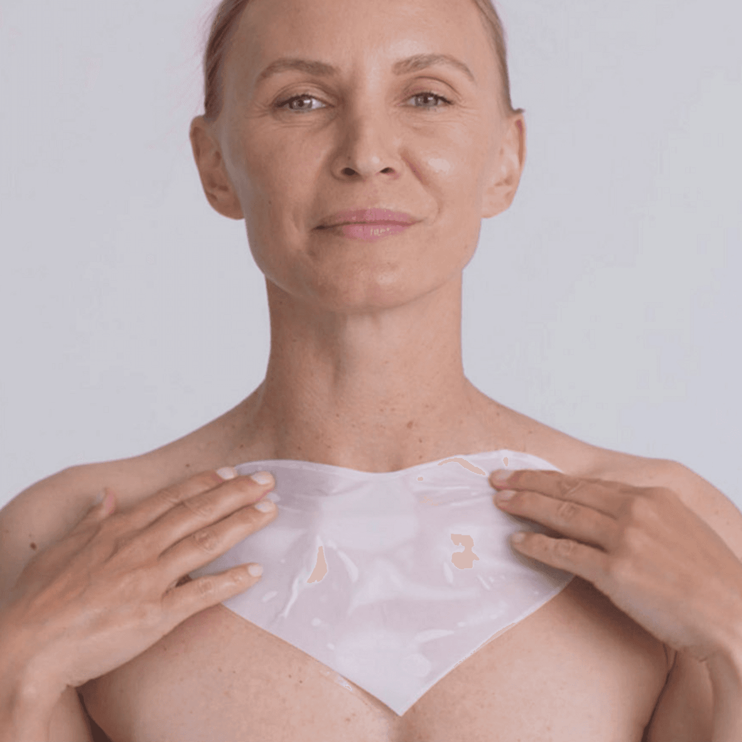 Woman applying Omnilux Hydrogel Decollete Mask Body Treatment to chest area for hydration and skin rejuvenation.