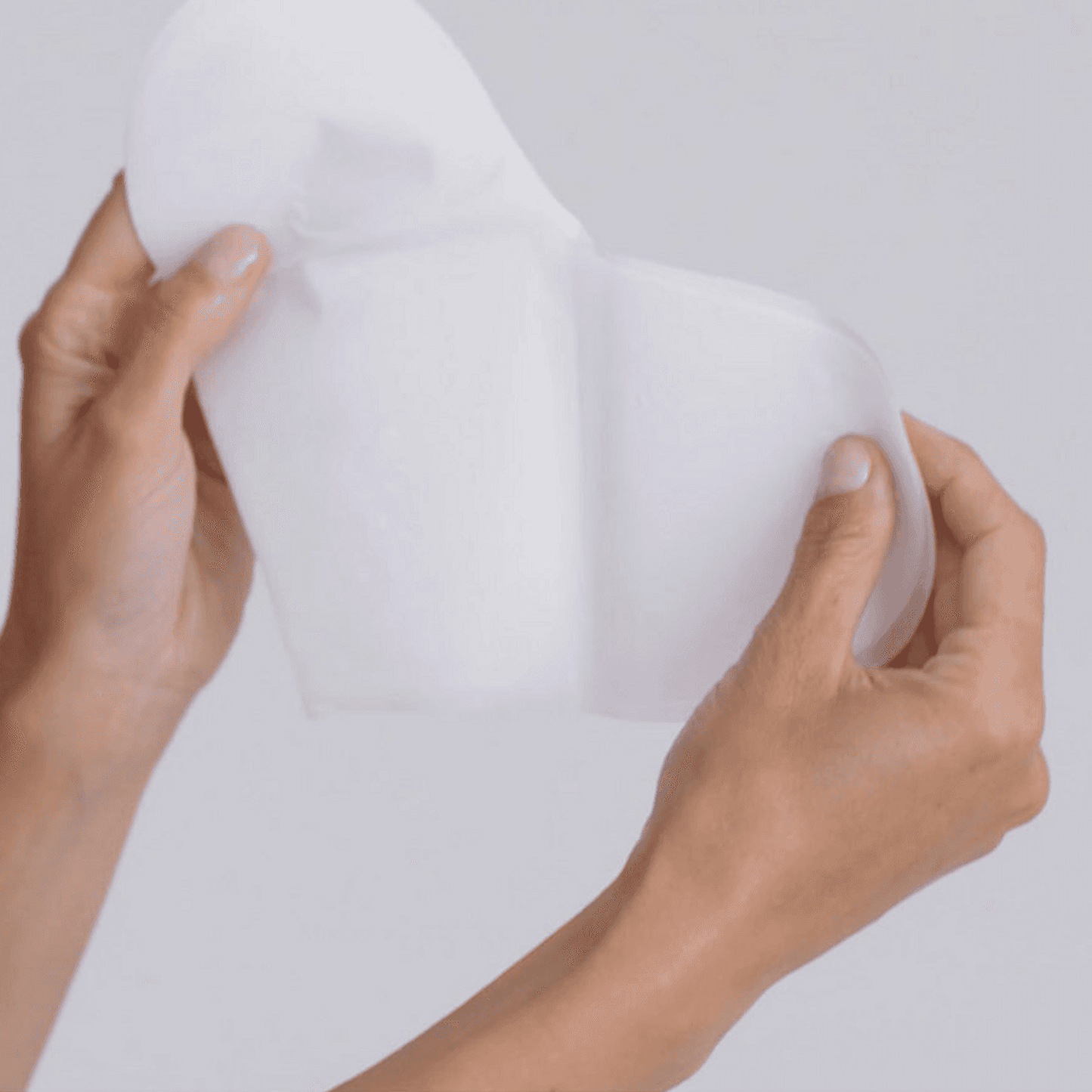 Hands holding Omnilux Hydrogel Decollete Mask Body Treatment showing flexible, soft texture for easy application.