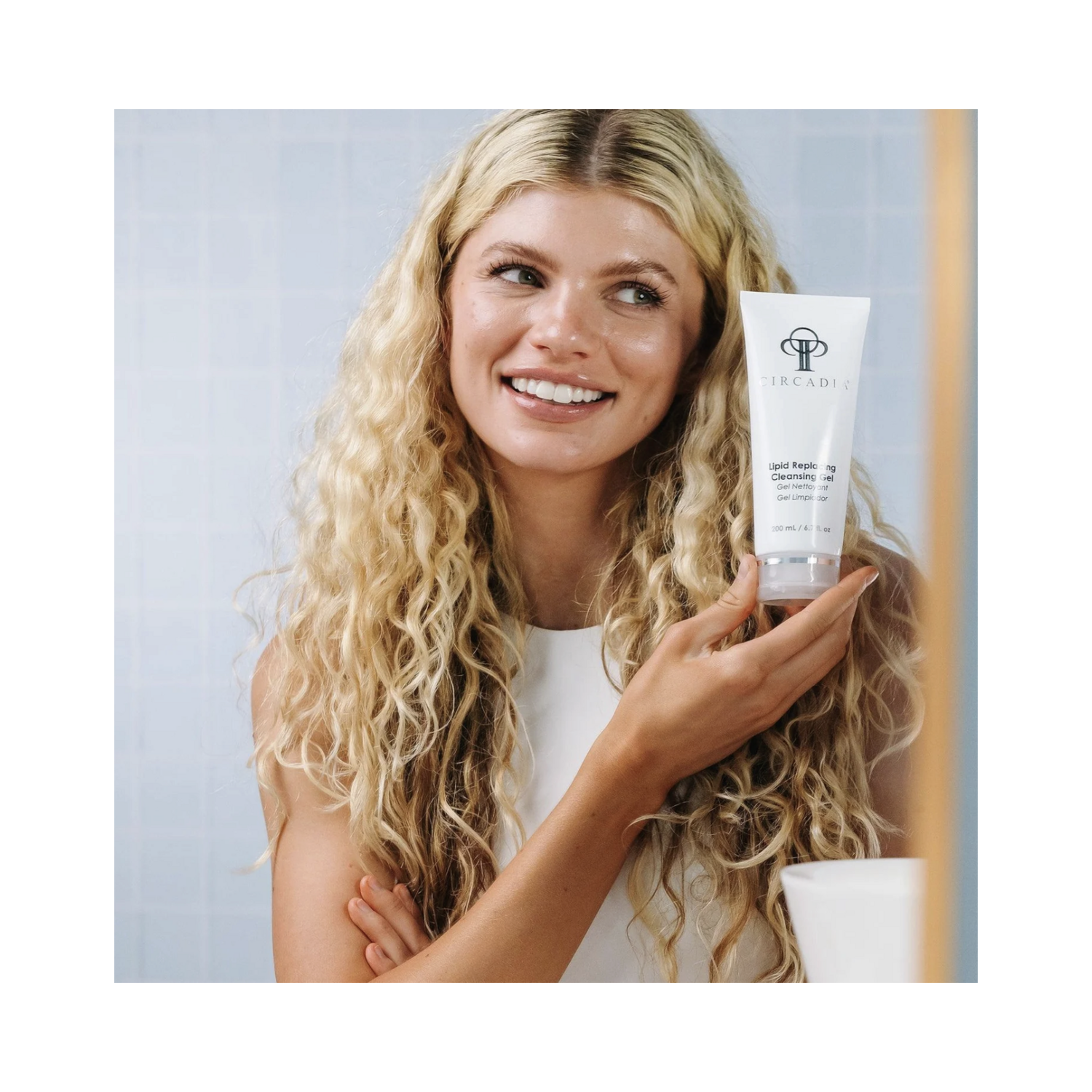 Smiling woman holding Circadia Lipid Replacing Cleansing Gel, highlighting its use in daily skincare for sensitive and dry skin types.