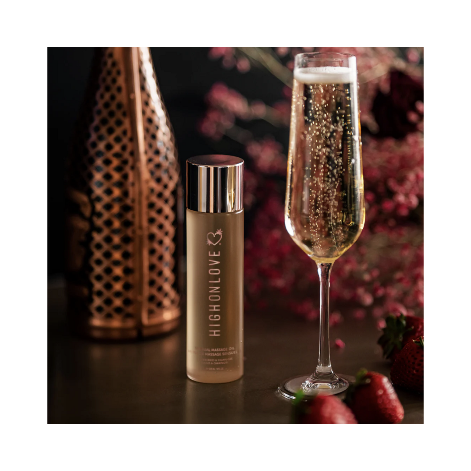 High on Love Massage Oil Topical Sunset Body Oil next to a champagne flute and strawberries, showcasing its sensual and pampering qualities.