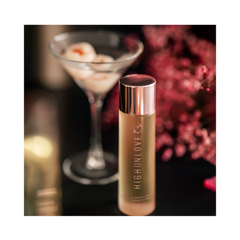 High on Love Massage Oil Topical Sunset Body Oil beside a martini glass and pink flowers, highlighting its romantic and luxurious appeal.