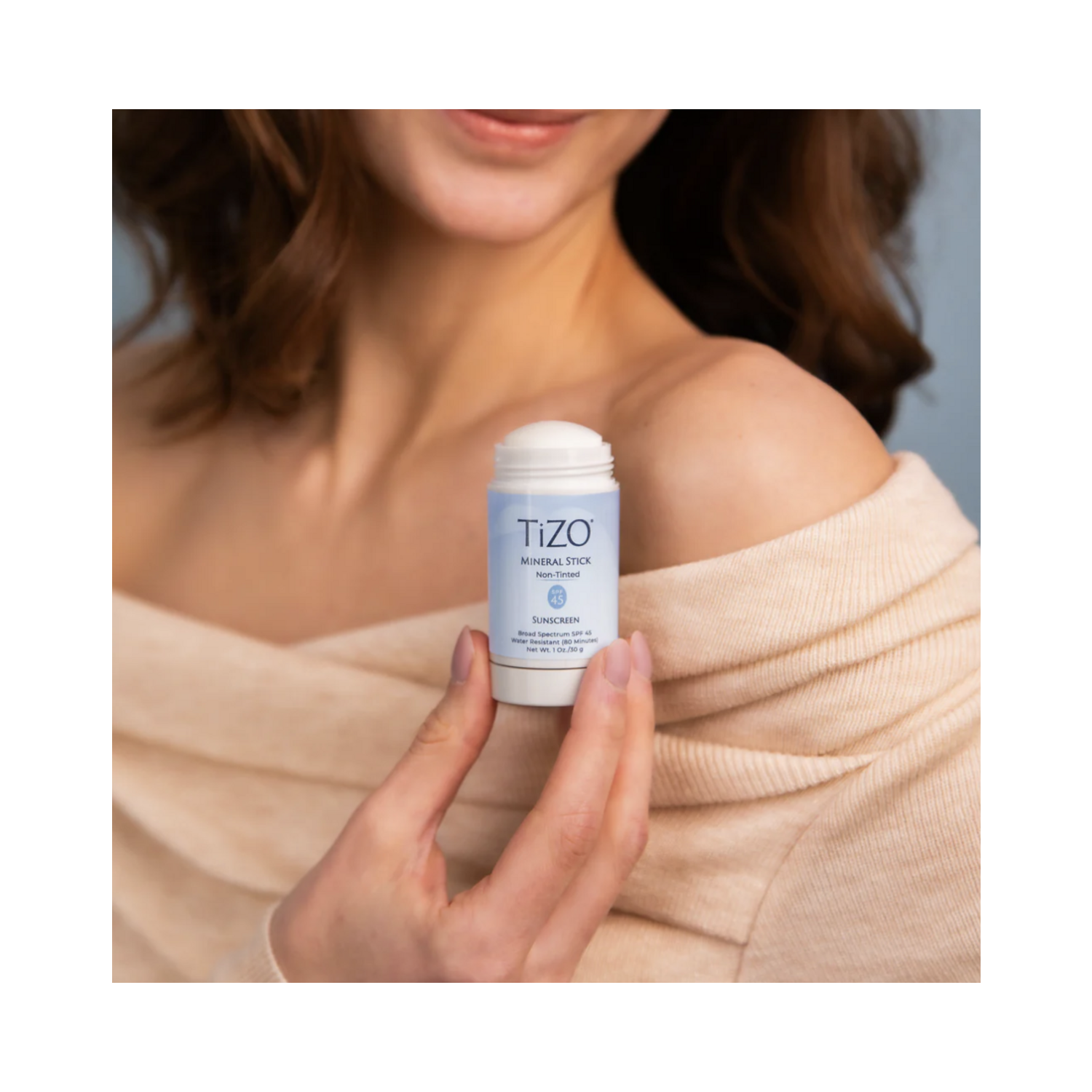 Model holding TiZO Mineral Stick Non Tinted Sunscreen near shoulder, emphasizing ease of use and compact size for daily skincare.
