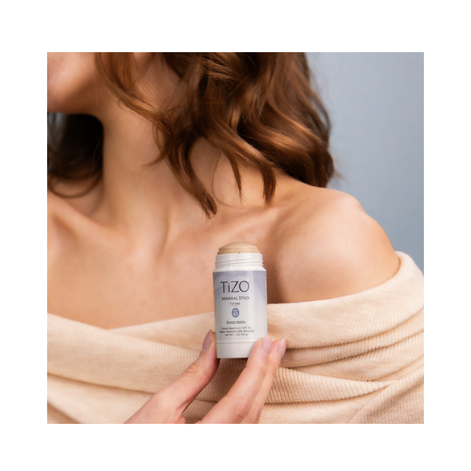 Woman applying TiZO Mineral Stick Tinted SPF 45 to shoulder, showcasing ease of use and skin-friendly formulation.