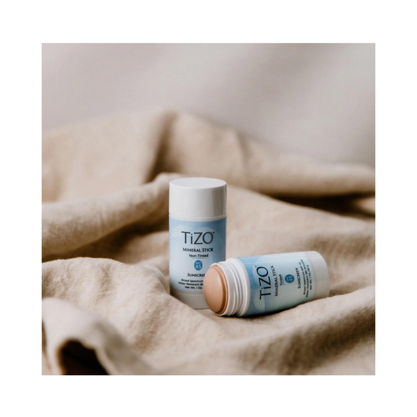 TiZO Mineral Stick Tinted SPF 45 shown open and closed on beige fabric, emphasizing its sleek, travel-ready packaging.