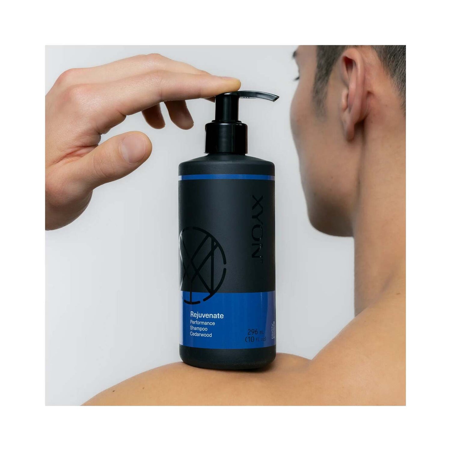 Man holding XYON Rejuvenate Men's Performance Shampoo on shoulder, highlighting product use for healthier, fuller hair with cedarwood scent.